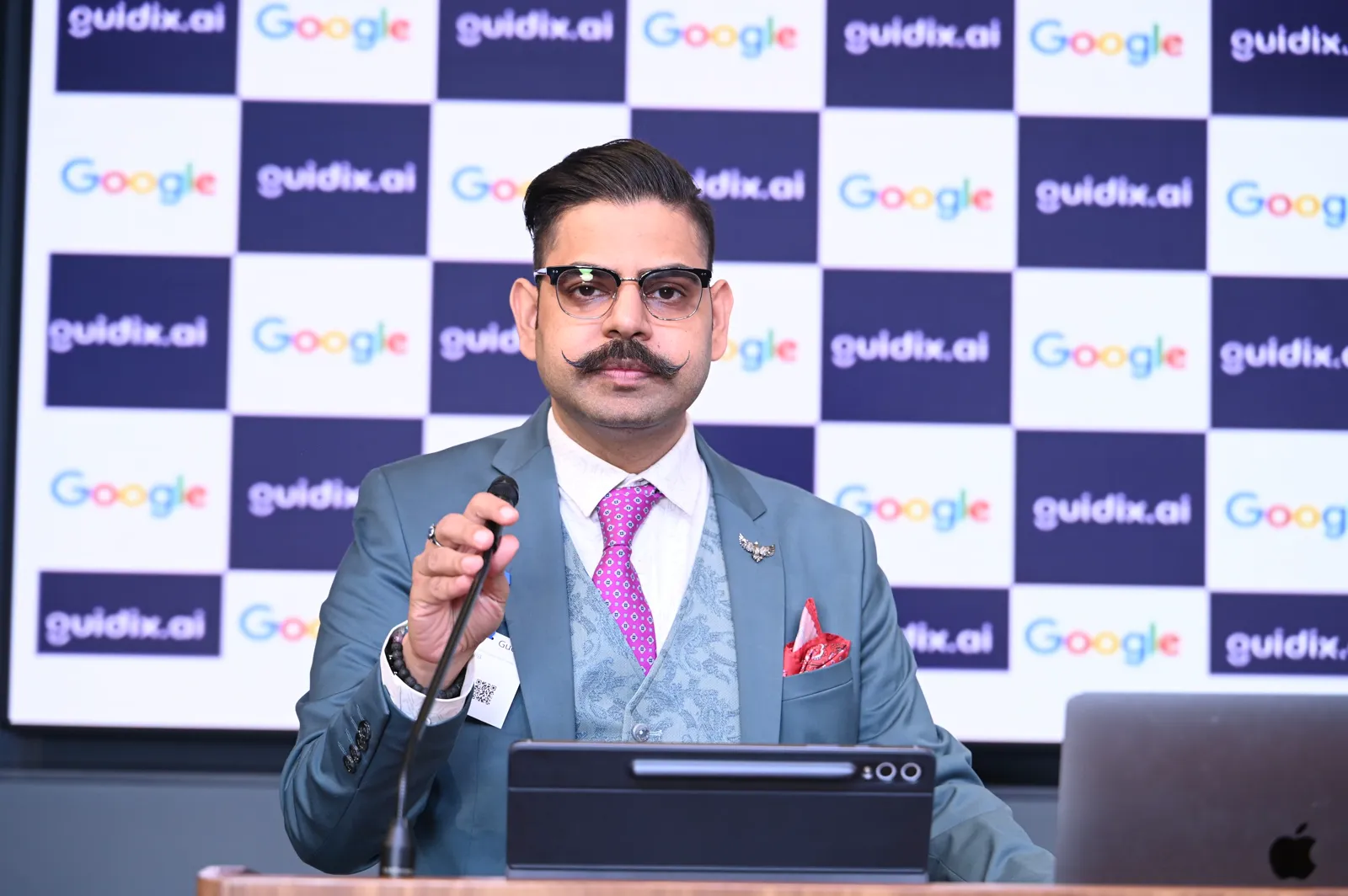 Speaker at the podium in front of the Google and guidix.ai branded backdrop